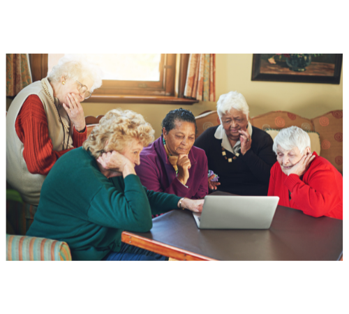 Five older ladies sitting at table looking at laptop