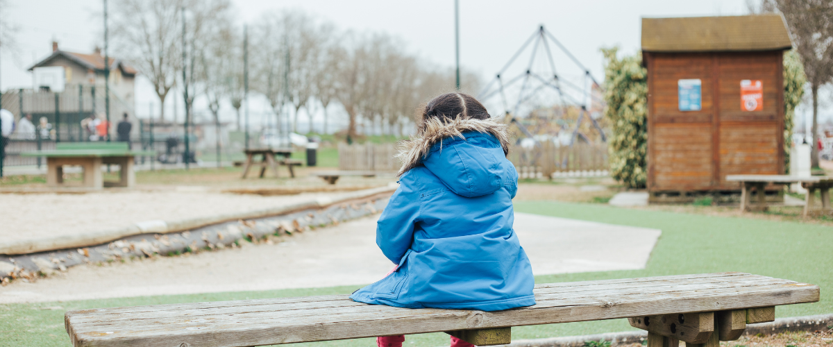 Little girl sitting on bench alone at playground